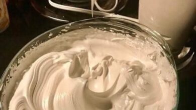 A bowl of creamy, freshly whipped buttercream frosting ready to be piped onto cakes and cupcakes, surrounded by a variety of decorative sprinkles