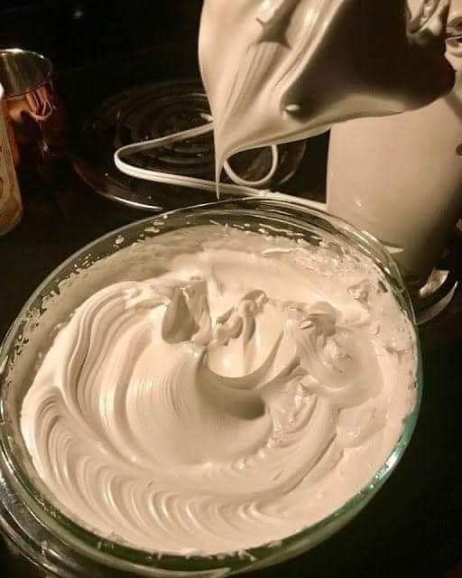A bowl of creamy, freshly whipped buttercream frosting ready to be piped onto cakes and cupcakes, surrounded by a variety of decorative sprinkles