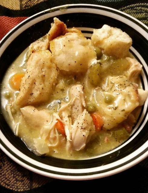 A steaming bowl of Crockpot Chicken and Dumplings, featuring tender chicken and fluffy dumplings, served in a rustic kitchen setting, ready to comfort and satisfy with its hearty flavors