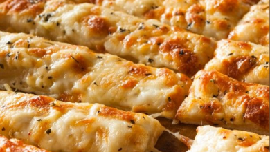 Deliciously golden Cheesy Garlic Breadsticks fresh out of the oven, served on a rustic wooden board, accompanied by bowls of marinara, ranch, and three-cheese dip, perfect for dipping