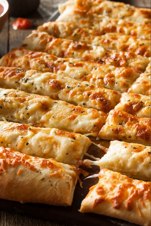 Deliciously golden Cheesy Garlic Breadsticks fresh out of the oven, served on a rustic wooden board, accompanied by bowls of marinara, ranch, and three-cheese dip, perfect for dipping
