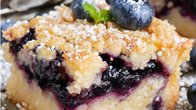 Freshly baked Blueberry Buckle in a rustic kitchen setting, topped with a golden brown sugar crust and served with a scoop of vanilla ice cream, creating an inviting and traditional dessert experience