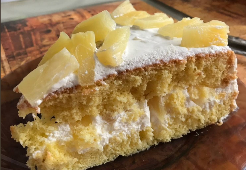 A lush and moist Pineapple Cake on a serving plate, garnished with fresh pineapple slices and a creamy frosting, perfectly embodying a tropical dessert paradise