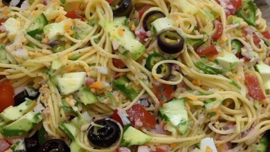 A vibrant California Spaghetti Salad served in a large white bowl, featuring al dente spaghetti mixed with cherry tomatoes, cucumbers, and bell peppers, drizzled with a homemade herbed dressing, perfect for a sunny California-inspired meal