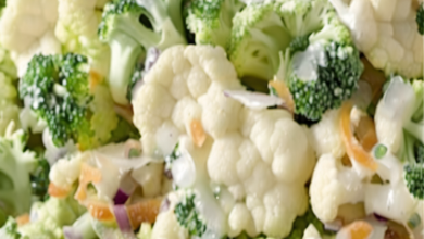 A colorful and refreshing broccoli and cauliflower salad in a large serving bowl, garnished with crispy bacon and shredded cheddar cheese, ready to be served at a family gathering or outdoor picnic