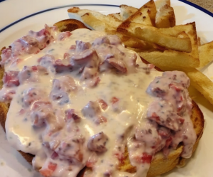 A plate of creamy chipped beef on toast garnished with freshly cracked black pepper, served on a rustic wooden table