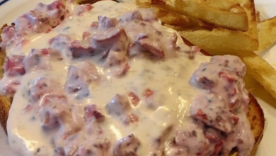 A plate of creamy chipped beef on toast garnished with freshly cracked black pepper, served on a rustic wooden table