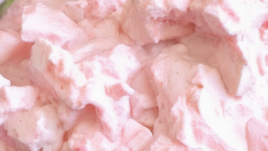 A close-up of a glass bowl filled with Rhubarb Fluff, showcasing its creamy texture and vibrant pink color, garnished with a fresh strawberry and a mint leaf.