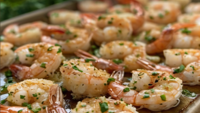 Close-up of succulent garlic parmesan shrimp on a baking sheet, garnished with fresh parsley and lemon slices, highlighting the rich, golden sauce.