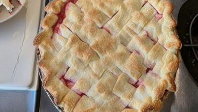 A beautifully baked Strawberry Rhubarb Pie with a golden crust, dotted with butter and sugar, cooling on a kitchen counter next to fresh strawberries and rhubarb stalks.