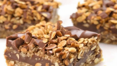 A tray of no-bake chocolate oat bars with a rich, chocolate layer in the middle, topped with a crumbly oat mixture and a drizzle of melted chocolate