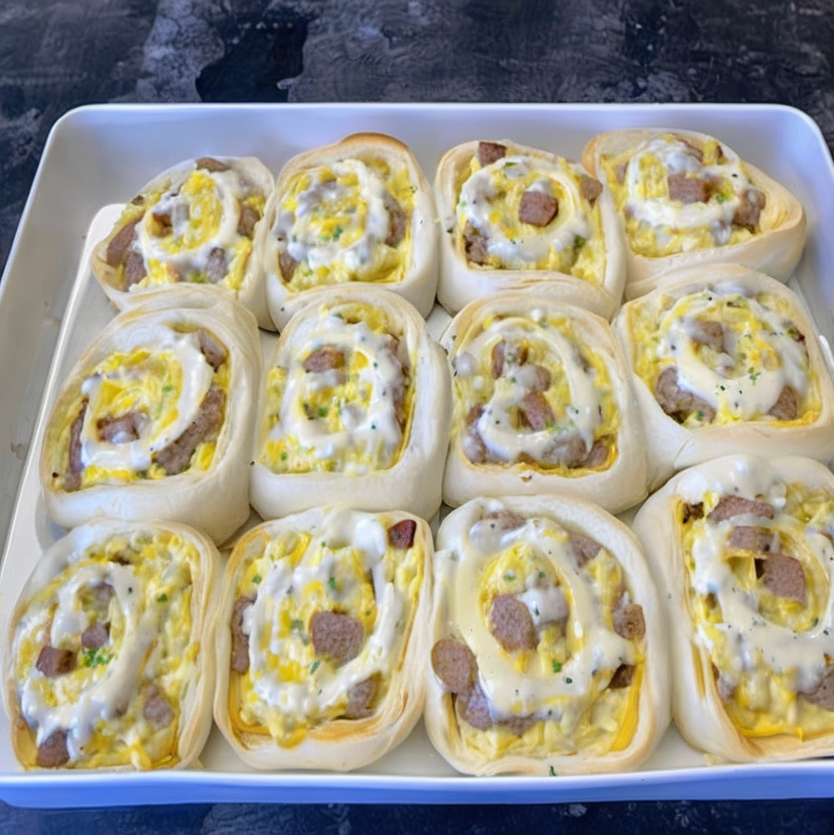 Golden brown breakfast rolls filled with sausage, egg, and cheese, topped with creamy sausage gravy, served on a white plate