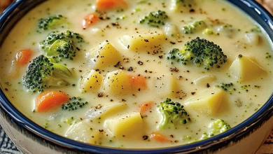 A creamy bowl of broccoli and potato soup, sprinkled with cheddar cheese and fresh herbs, served with a slice of whole-grain bread