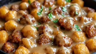 A hearty breakfast bowl filled with crispy tater tots, scrambled eggs, savory sausage, and creamy gravy, topped with chopped green onion