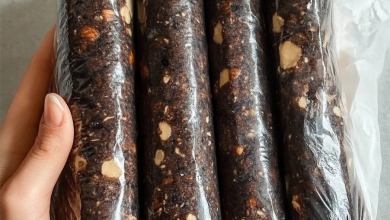 A sliced chocolate salami coated in powdered sugar, revealing pieces of cookies and walnuts inside. Perfect for parties or holiday gatherings.