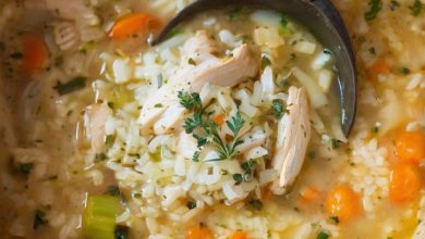 A cozy image of a bowl of chicken rice soup on a rustic table with a soft-focus background of a warm kitchen, highlighting the homey and comforting nature of the dish