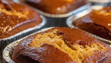 A freshly baked loaf of homemade cinnamon-sugar sweet bread on a wooden cutting board, sliced to show its soft, fluffy interior. The bread is topped with a glistening cinnamon-sugar coating that adds a golden-brown, slightly crunchy texture. Surrounding the loaf are a few cinnamon sticks and a small bowl of sugar, highlighting the bread’s warm, cozy flavors