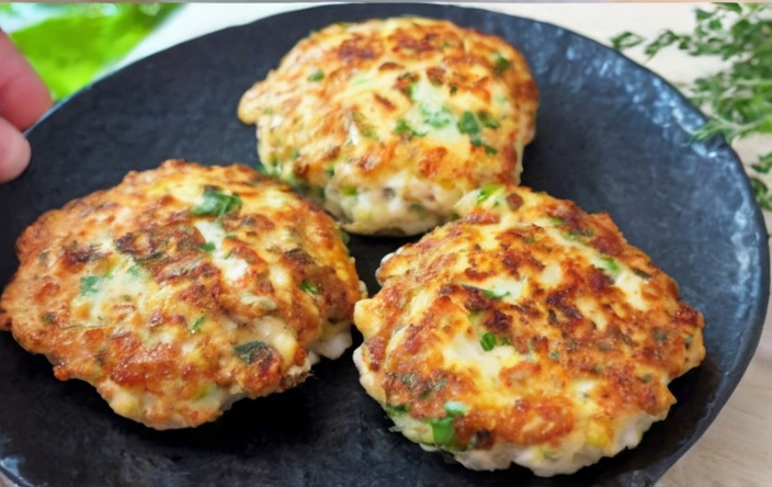 A vibrant close-up of golden-brown chicken burgers on a serving plate, garnished with fresh parsley and paired with a side of mixed greens, cherry tomatoes, and a lemon wedge for an added pop of color.