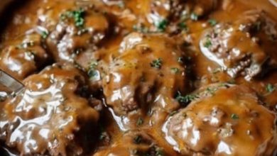 A hearty plate featuring golden-brown steak patties smothered in creamy mushroom gravy, served with fluffy mashed potatoes and a side of steamed green beans. A sprinkle of fresh parsley adds a pop of color