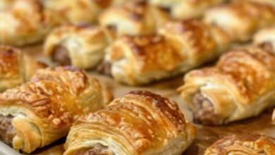 A golden tray of freshly baked crescent rolls, their glossy tops sprinkled with parsley and oozing creamy cheese and savory sausage filling. Served alongside small bowls of dipping sauces, this image screams indulgence and satisfaction.