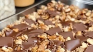 A close-up shot of perfectly cut Caramel Chocolate Crunch Bars arranged on a wooden tray, showcasing the glossy chocolate top, gooey caramel layer, and crunchy pretzel base. Garnished with a light sprinkle of sea salt for a touch of elegance.