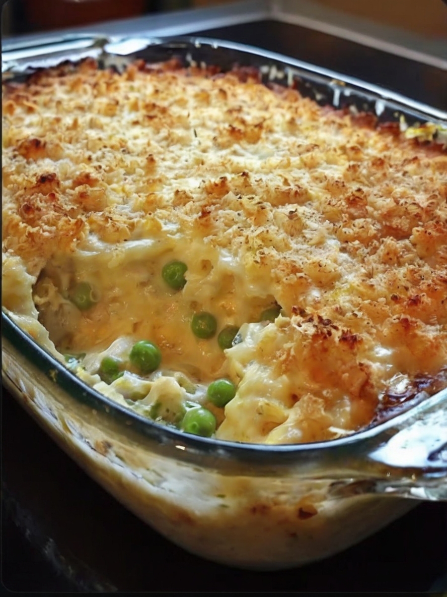 A freshly baked hashbrown chicken casserole sits in a glass baking dish, topped with golden-brown breadcrumbs, melted cheese, and garnished with chopped parsley. A serving spoon is placed next to the dish, and a side salad in the background adds a touch of freshness.