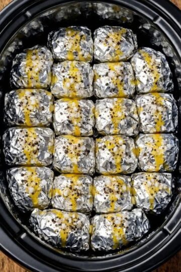 Individually foil-wrapped russet potatoes steamed to fork-tender perfection in the slow cooker, then stuffed with molten sharp cheddar and crispy bacon. Each potato gets infused with butter and seasonings during the long, gentle cook, then finished with a gooey cheese-and-bacon center. The ultimate hands-off side dish with dramatic tableside appeal.