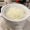 "Thinly sliced onions filling a white slow cooker on a kitchen countertop, ready to cook into sweet caramelized onions in a Crock-Pot."