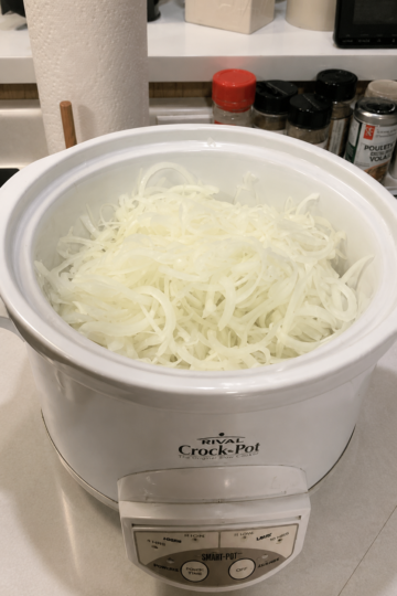 "Thinly sliced onions filling a white slow cooker on a kitchen countertop, ready to cook into sweet caramelized onions in a Crock-Pot."