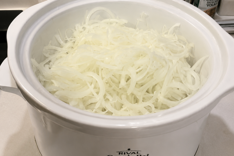 "Thinly sliced onions filling a white slow cooker on a kitchen countertop, ready to cook into sweet caramelized onions in a Crock-Pot."