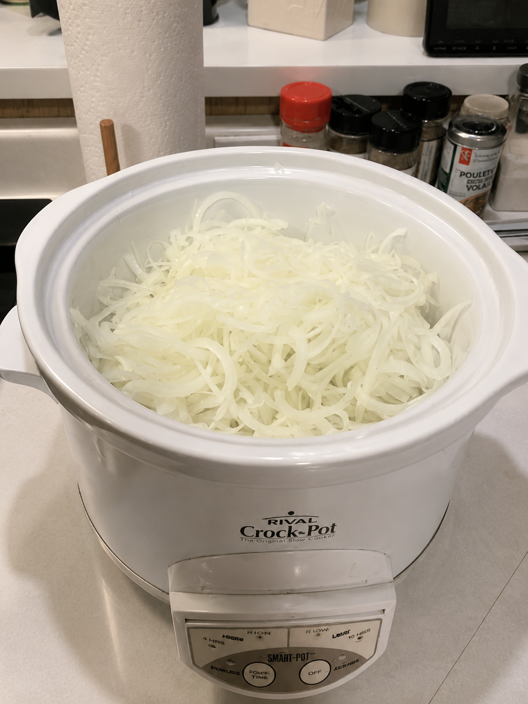 "Thinly sliced onions filling a white slow cooker on a kitchen countertop, ready to cook into sweet caramelized onions in a Crock-Pot."