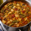 Hearty vegetable beef soup in a warm bowl with tender beef chunks, diced potatoes, carrots, celery, green beans, corn, tomatoes, and fresh parsley in a rich savory broth.