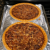 Classic pecan pie in a flaky deep-dish crust with glossy caramel filling, toasted pecan pieces, golden edges, and a rich buttery holiday dessert texture.