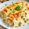 A baking dish filled with creamy white chicken enchiladas topped with melted golden Monterey Jack cheese and baked until bubbly. The soft flour tortillas are stuffed with tender shredded chicken and covered in a rich sour cream and green chile sauce, then garnished with fresh cilantro for a comforting American family dinner.