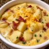 Old-Fashioned Loaded Potato Soup topped with crispy bacon, shredded sharp cheddar cheese, sour cream, diced ham, and fresh green onions in a rustic bowl. This rich and creamy homemade potato soup is the ultimate American comfort food, perfect for cozy family dinners, cold winter nights, and hearty lunch recipes.