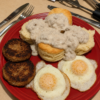 Southern biscuits and sausage gravy breakfast plate with fluffy buttermilk biscuits covered in creamy peppered sausage gravy, crispy sausage patties, and fried eggs.