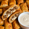 "Crispy cheeseburger egg rolls filled with seasoned ground beef and melted cheese, served with a creamy dipping sauce for an easy homemade appetizer