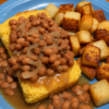 Southern pinto beans served over golden cornbread with caramelized onions and crispy fried potatoes on the side, a classic comfort food plate with rich bean broth.