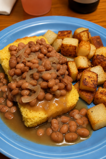Southern pinto beans served over golden cornbread with caramelized onions and crispy fried potatoes on the side, a classic comfort food plate with rich bean broth.