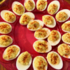 "Classic deviled eggs arranged on a red serving tray, filled with creamy seasoned yolk mixture and sprinkled with paprika for a traditional homemade appetizer