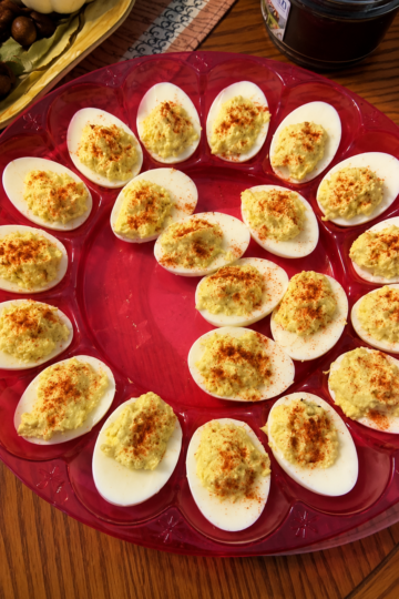 "Classic deviled eggs arranged on a red serving tray, filled with creamy seasoned yolk mixture and sprinkled with paprika for a traditional homemade appetizer
