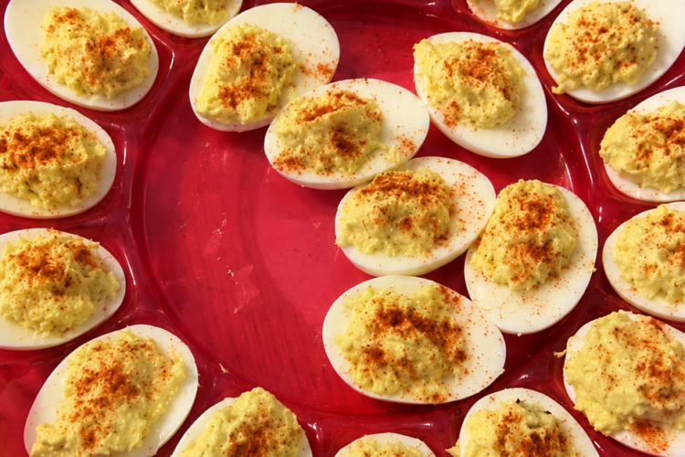 "Classic deviled eggs arranged on a red serving tray, filled with creamy seasoned yolk mixture and sprinkled with paprika for a traditional homemade appetizer