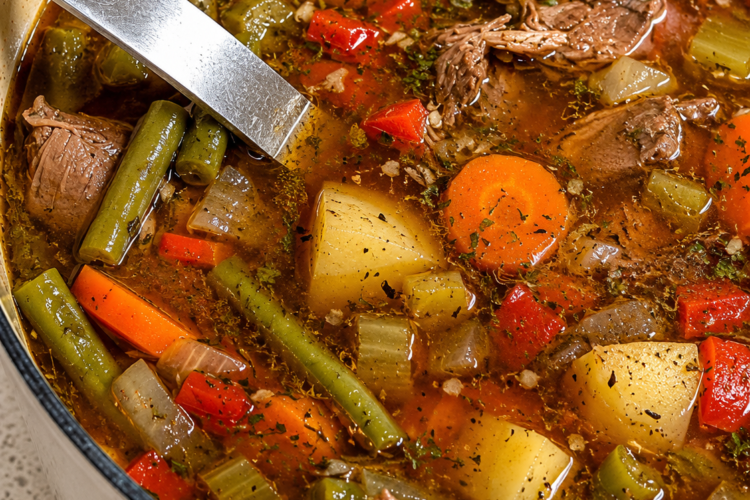 A steaming bowl of hearty vegetable beef soup filled with tender chunks of seared beef, diced carrots, potatoes, green beans, and corn in a rich savory broth, garnished with fresh chopped parsley.
