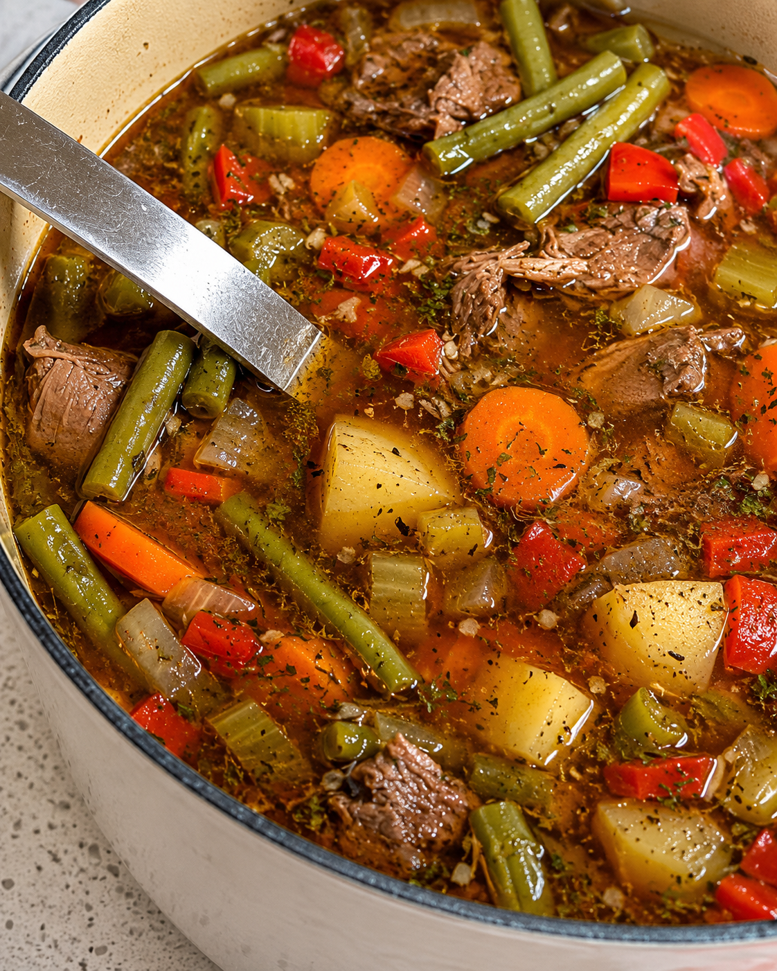 A steaming bowl of hearty vegetable beef soup filled with tender chunks of seared beef, diced carrots, potatoes, green beans, and corn in a rich savory broth, garnished with fresh chopped parsley.