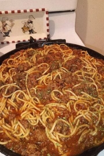 Classic homemade spaghetti topped with rich ground beef tomato sauce, garnished with fresh parsley and grated Parmesan cheese, served in a rustic bowl for a comforting American family dinner.