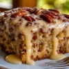 A moist Butter Pecan Praline Poke Cake topped with glossy homemade praline glaze and toasted pecan halves, served on a white dessert plate with extra caramel sauce drizzled over each slice. The buttery cake is soft, rich, and soaked with a sweet brown sugar praline filling, making it the perfect Southern-inspired holiday dessert.