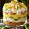 A beautiful Key Lime Pie Trifle layered in a clear glass trifle bowl with buttery graham cracker crumbs, creamy key lime cheesecake filling, fluffy homemade whipped cream, and thin lime slices. The no-bake dessert is topped with whipped cream, fresh lime zest, graham cracker crumbs, and lime wedges, making it a refreshing and elegant dessert for summer parties, holidays, and family gatherings.