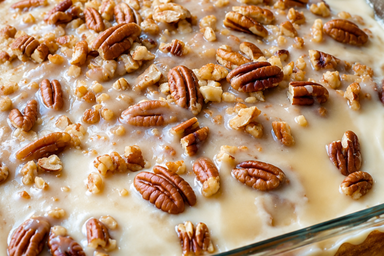 "Butter pecan poke cake topped with creamy vanilla glaze and generously sprinkled with chopped pecans, served in a glass baking dish for a classic Southern homemade dessert."