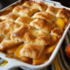Triple-layer peach cobbler baked golden in a 9x13 dish with sliced peaches, buttery crisp topping, bubbling peach syrup, and warm cinnamon-vanilla filling.