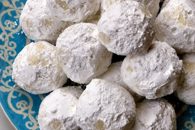 "Powdered sugar snowball cookies piled on a blue decorative plate, featuring buttery homemade cookies generously coated in confectioners' sugar."